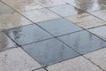 The urban street surface of the road is wet, the street is paved with square gray black granite tiles. Wet asphalt, rainy weather