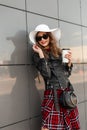 Urban stylish smiling woman in red-black fashionable clothes in sunglasses in white hat with tasty tea in city. Trendy girl with