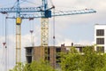 Urban view of silhouettes of two high industrial tower cranes working at construction of new brick building with workers in hard h Royalty Free Stock Photo