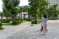 Urban walking road among green tree in modern apartment buildings in big city, with woman pushing baby stroller