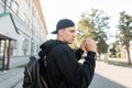 Urban young hipster man in a hooded sweatshirt in a baseball cap in sunglasses with a backpack is walks near a vintage building Royalty Free Stock Photo