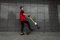 Urban young hipster man in stylish denim red-black clothes in sunglasses posing with a modern electric scooter Royalty Free Stock Photo