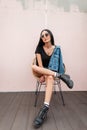 Urban young hipster woman in black leather boots in fashionable jeans clothes in stylish sunglasses posing on a straw chair Royalty Free Stock Photo