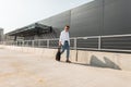 Urban young man hipster in stylish white and denim clothes in trendy sandals with a black cloth bag walks outdoors on a sunny day Royalty Free Stock Photo