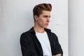 Urban young man with a stylish hairstyle in an elegant black shirt in a white T-shirt is standing near a vintage building Royalty Free Stock Photo