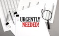 URGENTLY NEEDE text on paper on chart background Royalty Free Stock Photo