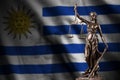 Uruguay flag with statue of lady justice and judicial scales in dark room. Concept of judgement and punishment