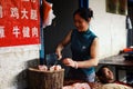young woman chopping meat at the local street market while her husband sleeping at the background