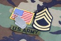 US ARMY Sergeant First Class rank patch, branch tape, flag patch and dog tags on woodland camouflag Royalty Free Stock Photo