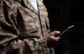 Young soldier holding a mobile phone standing on black background