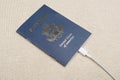 US citizen passport with white cable plugged into the passport on a beige textile backdrop in sunlight