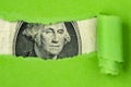 US currency peeking through torn green paper