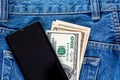 US dollar banknotes and smartphone over the left rear pocket of blue jeans. Royalty Free Stock Photo