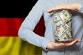 US dollars cash money in glass jar in hand on German flag background. Business, politics, banking and corruption concept Royalty Free Stock Photo