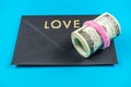 US dollars rolled up and tightened with colored band on light blue background.Sealed black envelop.Love Royalty Free Stock Photo