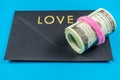 US dollars rolled up and tightened with colored band on light blue background.Sealed black envelop.Love Royalty Free Stock Photo
