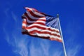 US flag, dynamically fluttering in the wind against a blue cloudy sky background.