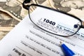 US 1040 individual tax return form, glasses and dollar bills with pen