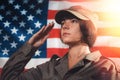 USA celebration. Portrait of a female soldier saluting, against the background of the American flag. Side view. Light Royalty Free Stock Photo