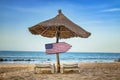 USA flag on wooden arrow sign. There are two sun loungers and a sun umbrella on the beach. It is a tropical paradise with a clear