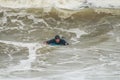 Surfer in the black swimsuit swimming lying on a blue surfing board in the stormy ocean