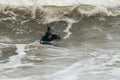 Surfer in the black swimsuit swimming lying on a blue surfing board in the stormy ocean