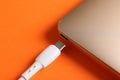 USB charge cable with lightning connector and laptop on orange background, closeup Royalty Free Stock Photo