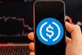 USD Coin USDC cryptocurrency logo on the screen of smartphone in mans hand with downtrend on the chart on a red light