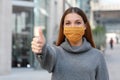 Use the mask! Young woman wearing protective mask showing thumbs up in city street