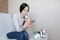 Use nebulizer and inhaler for the treatment. Young woman inhaling through inhaler mask and looking at phone. Side view.