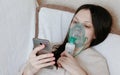 Use nebulizer and inhaler for the treatment. Young woman inhaling through inhaler mask lying on the couch and chatting Royalty Free Stock Photo