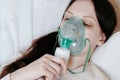 Use nebulizer and inhaler for the treatment. Young woman`s face inhaling through inhaler mask lying on the couch. Side