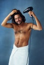 Use proper care to maintain great hair. Studio portrait of a handsome young man blowdrying his hair against a blue