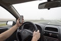 Use of smartphone in car. Man using phone while driving in fog on highway Royalty Free Stock Photo