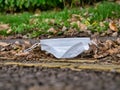 A used, blue surgical face mask used for COVID-19 PPE protection, discarded as litter on a pavement / sidewalk Royalty Free Stock Photo