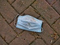A used, blue surgical mask used for COVID-19 PPE protection, discarded as litter on a pavement / sidewalk in an urban area Royalty Free Stock Photo