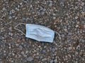 A used, blue surgical mask used for COVID-19 PPE protection, discarded as litter on a pavement / sidewalk Royalty Free Stock Photo