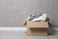 Used clothes in cardboard box on floor near grey wall. Space for text Royalty Free Stock Photo