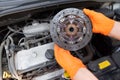 Auto mechanic wearing protective work gloves holds used clutch disc friction plate over a car engine