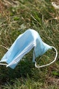 A used disposable blue face mask carelessly discarded on grass, during the Covid-19 pandemic