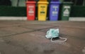 Used medical face mask discard on pavement floor on blurred recycle bin or trash. Medical waste disposal with unhygienic.