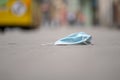 A used medical mask is lying on the sidewalk in the city against the blurry background of passing traffic, close-up, selective foc