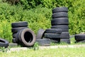 Used old car tyres stacked together next to overgrown curb ready for recycling at local tyre shop backyard surrounded with dense