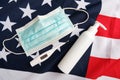 Used protective mask, digital thermometer and sanitizer pump bottle on american flag background.