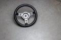 small racing steering wheel with black leather made of aluminum on a polished concrete floor, used steering wheel, a sign for