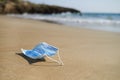 Used surgical mask thrown on the sand of a beach