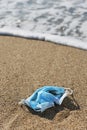 Used surgical mask thrown on the sand of a beach