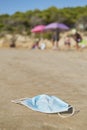 Used surgical mask thrown on the sand of a beach