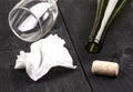 The used white crumpled paper napkin and an empty wine bottle with cork on old wooden table