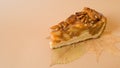 Useful baking. An appetizing piece of apple pie with pecans on autumn leaves on a plain light brown background